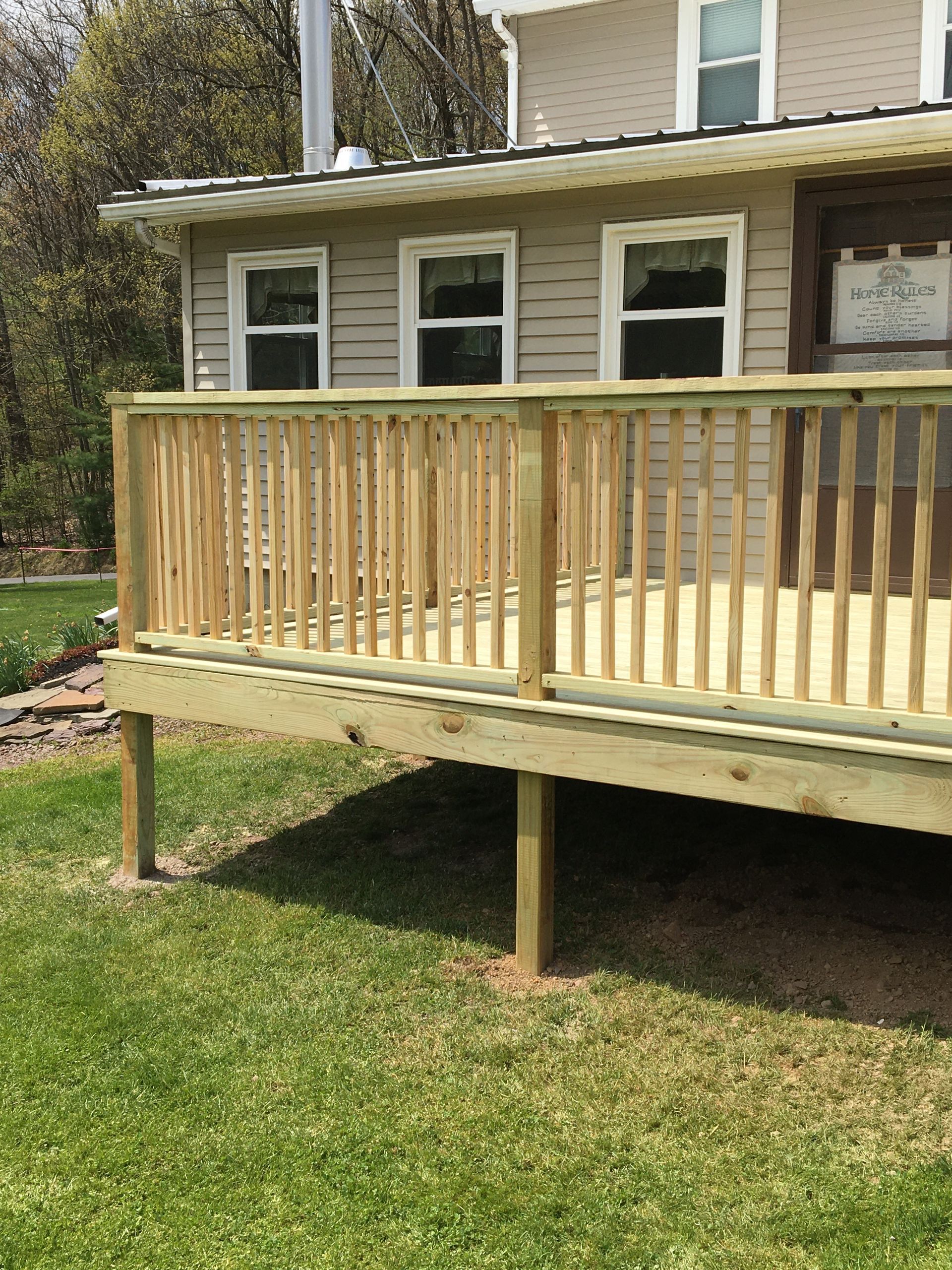 A new wooden deck with vertical balusters attached to the side of a beige, multi-story house.