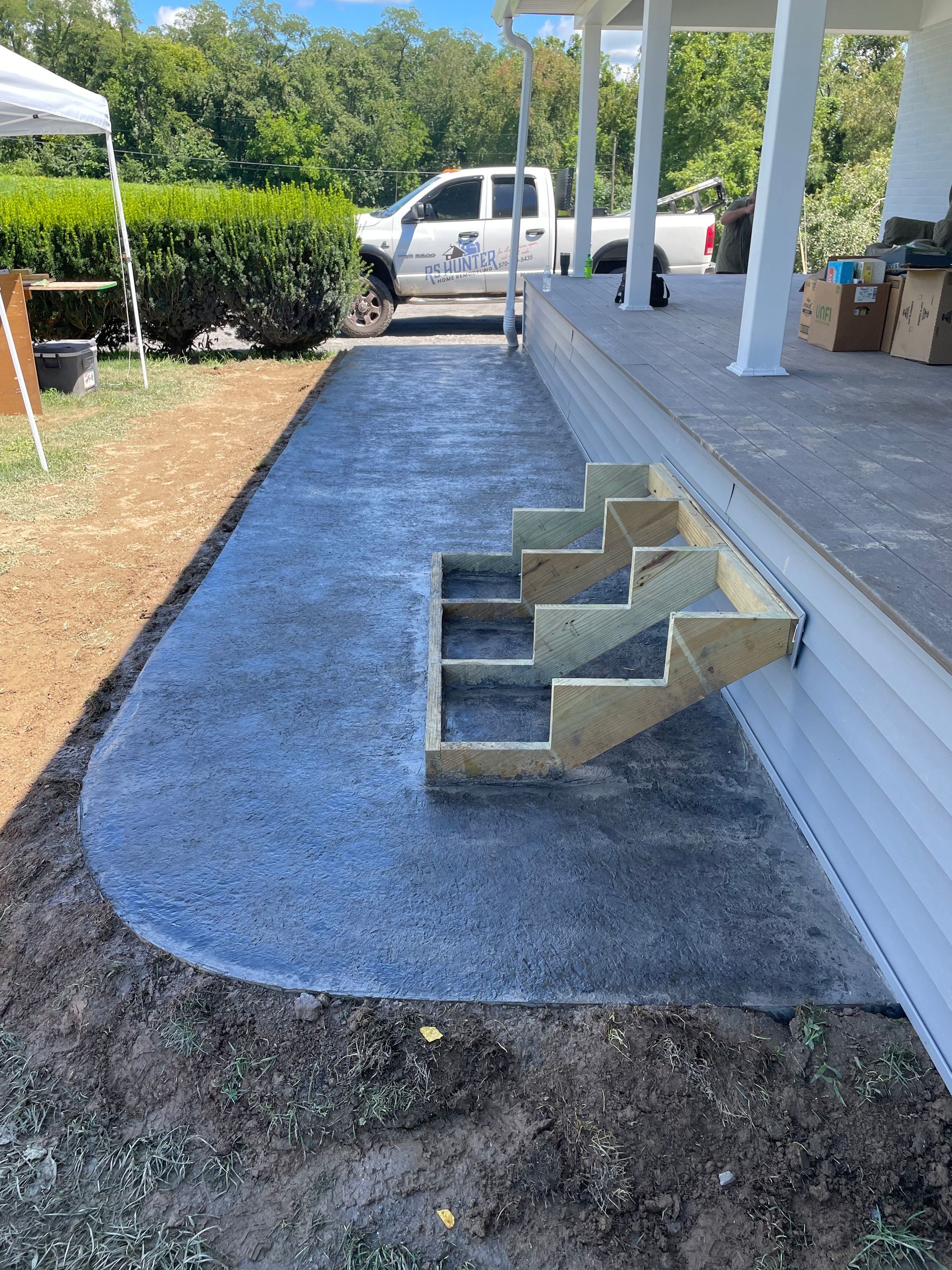 A newly poured concrete walkway alongside a house porch with unfinished wooden stair stringers.