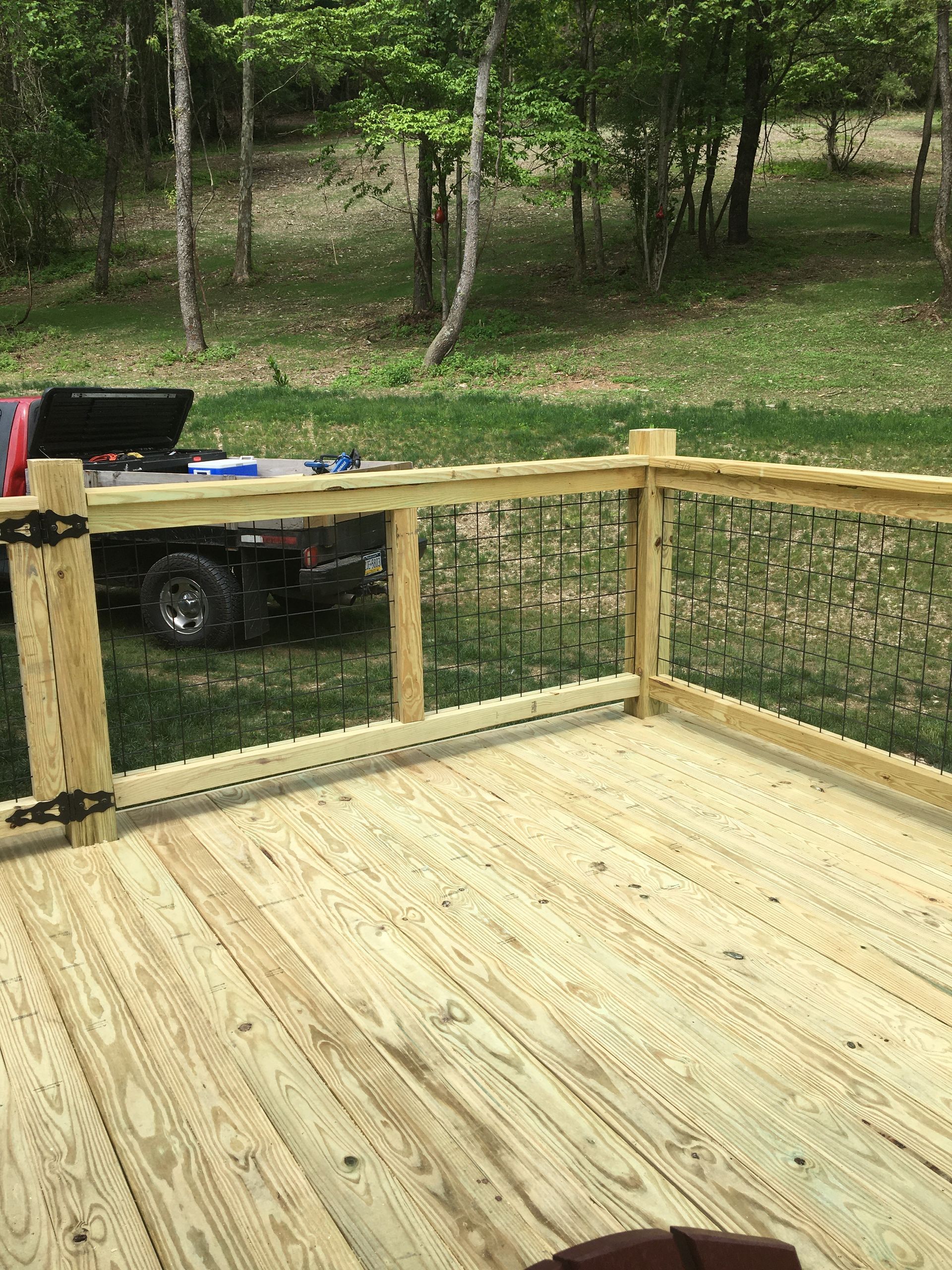 Newly constructed light-colored wooden deck railing with thin metal balusters, overlooking a grassy, wooded yard.