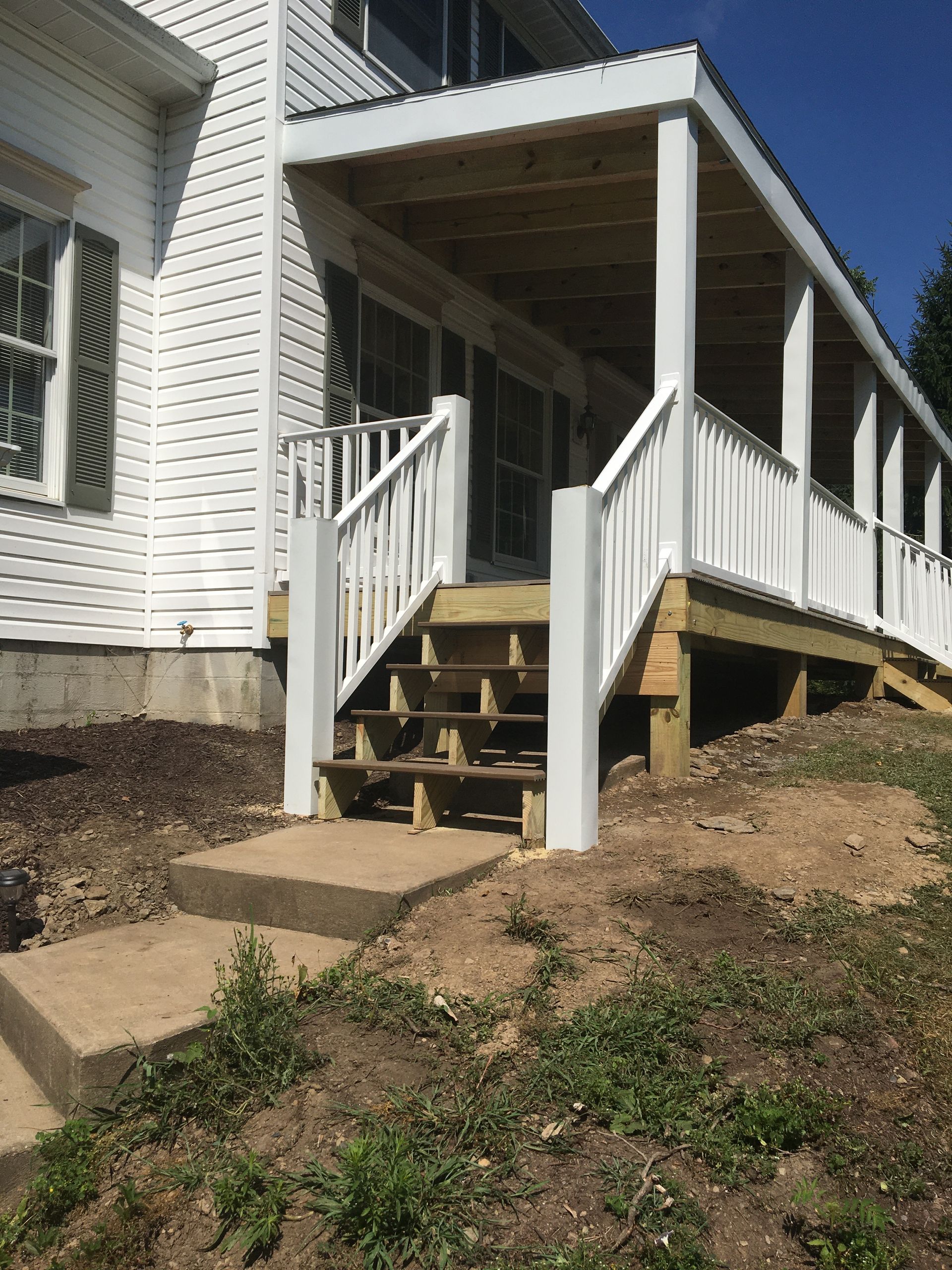 A white house with a newly constructed wooden porch, featuring white railings and unfinished wooden steps.