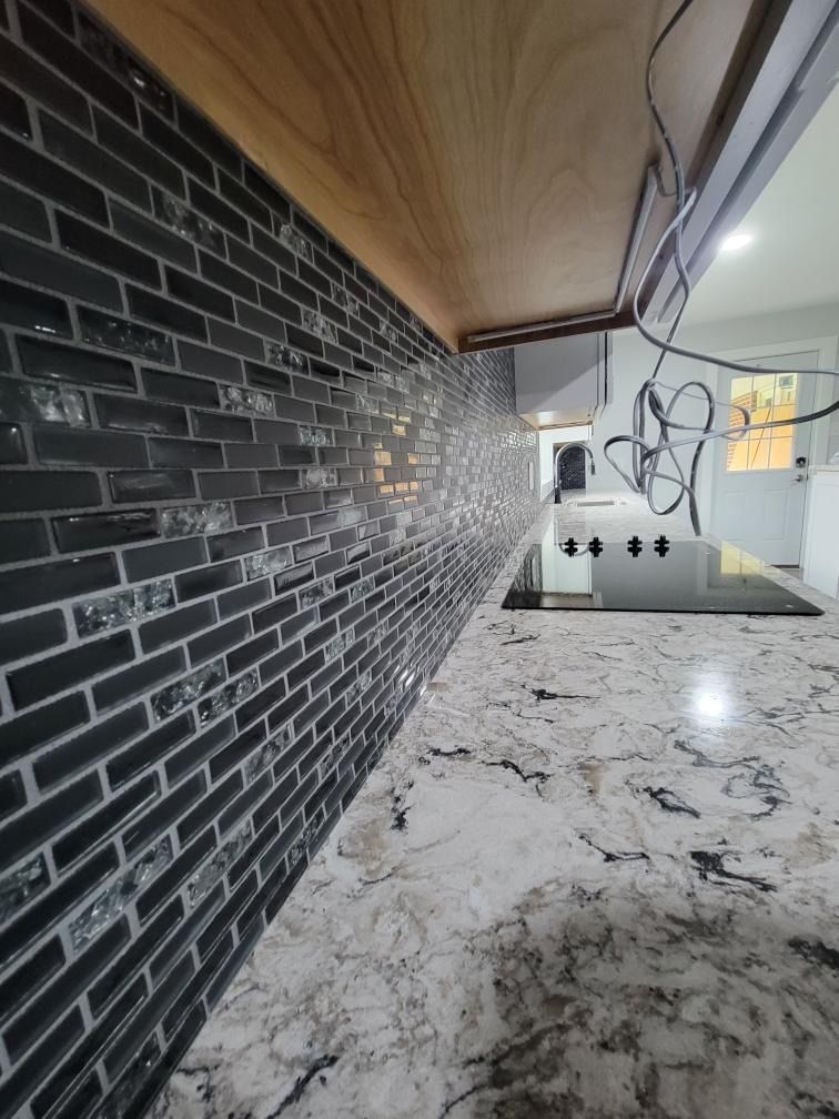 A kitchen backsplash with dark, narrow brick-style tiles above a white and black speckled granite countertop.