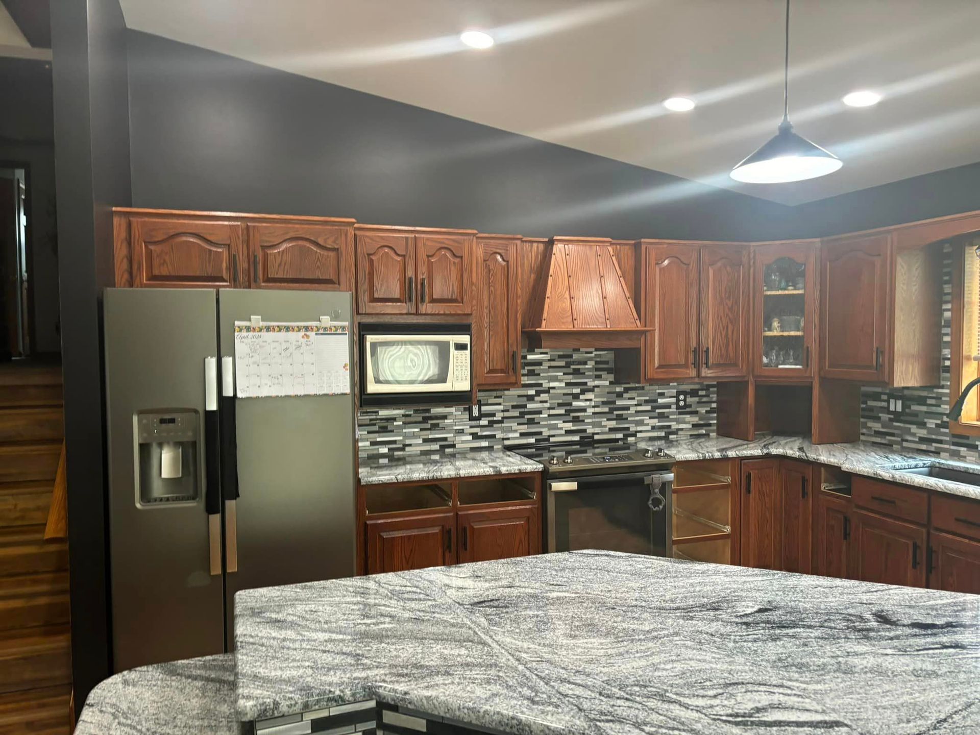 A kitchen with wooden cabinets, a gray refrigerator, a patterned backsplash, and a large gray and white granite island.