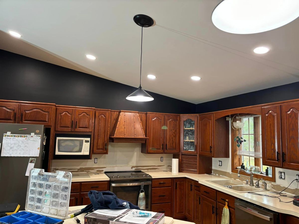 A kitchen with wood cabinetry, dark painted walls, a pendant light, and a sloped ceiling with recessed lighting.
