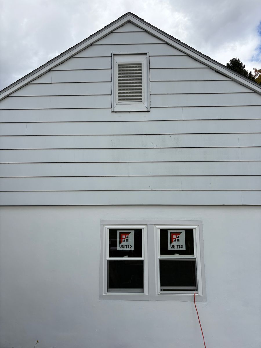Exterior view of a white, gabled house with horizontal siding, an attic vent, and a newly installed window.