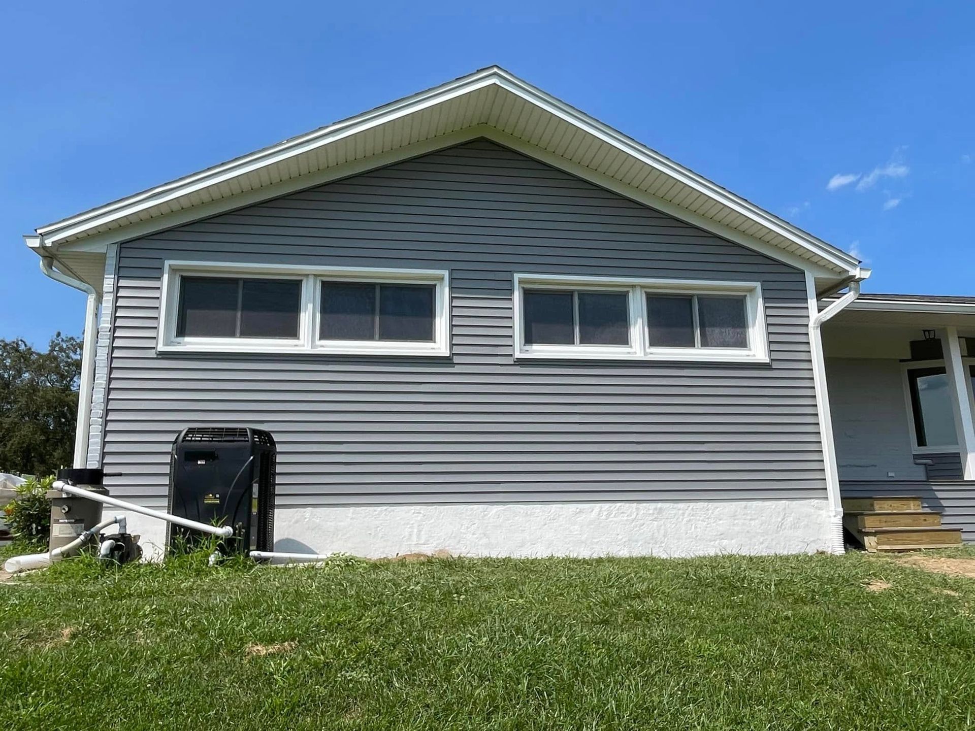 A side view of a gray, vinyl-sided house with four rectangular windows, set against a bright blue sky.