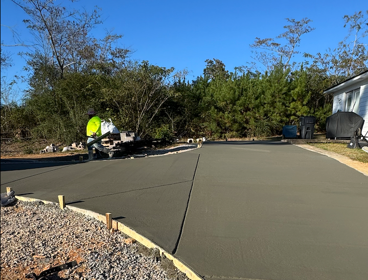 Newly poured concrete driveway with a worker in the background, blue sky.