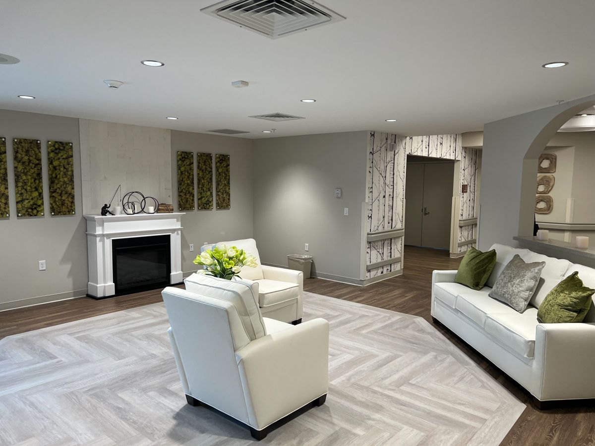 Cozy living room with fireplace, white armchairs, and sofa, accented by green pillows, on a neutral patterned carpet.