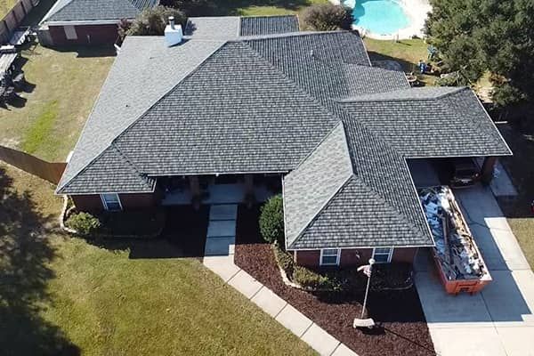 Aerial view of a house with gray shingles, a pool, and a dumpster in the driveway.