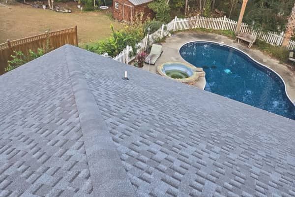 View of a gray shingled roof with a pool and backyard in the background.