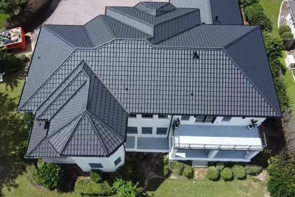 Aerial view of a white house with a dark gray metal roof surrounded by greenery.