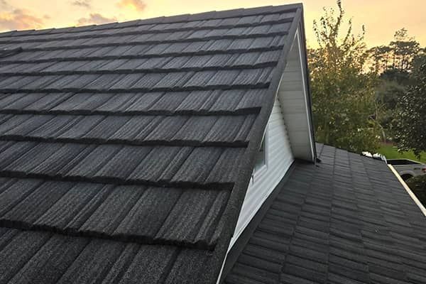 Dark gray metal tile roof on a house, angled view, overcast sky.