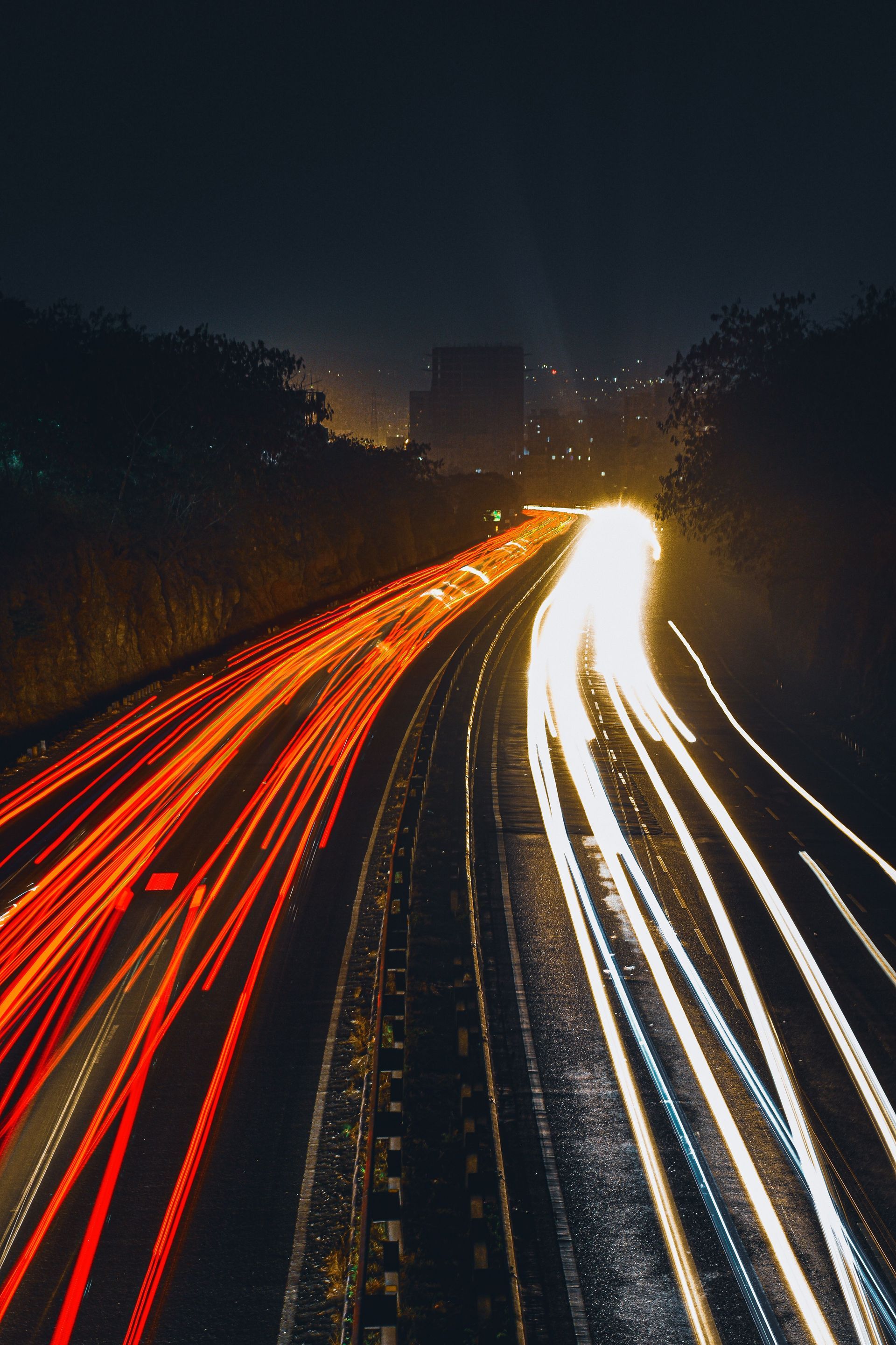 Een snelweg 's nachts met rode en witte lichtsporen van auto's die in de verte verdwijnen.