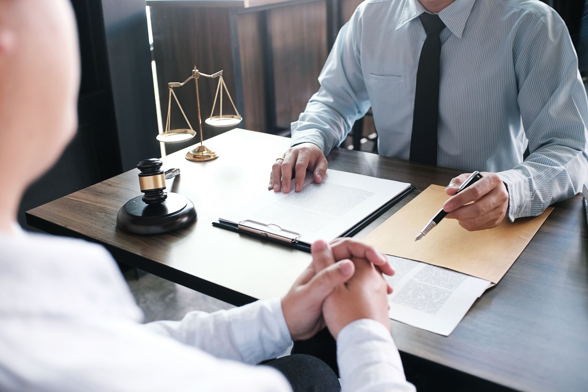 A lawyer with a gavel and scales of justice consulting a client across a desk with legal documents