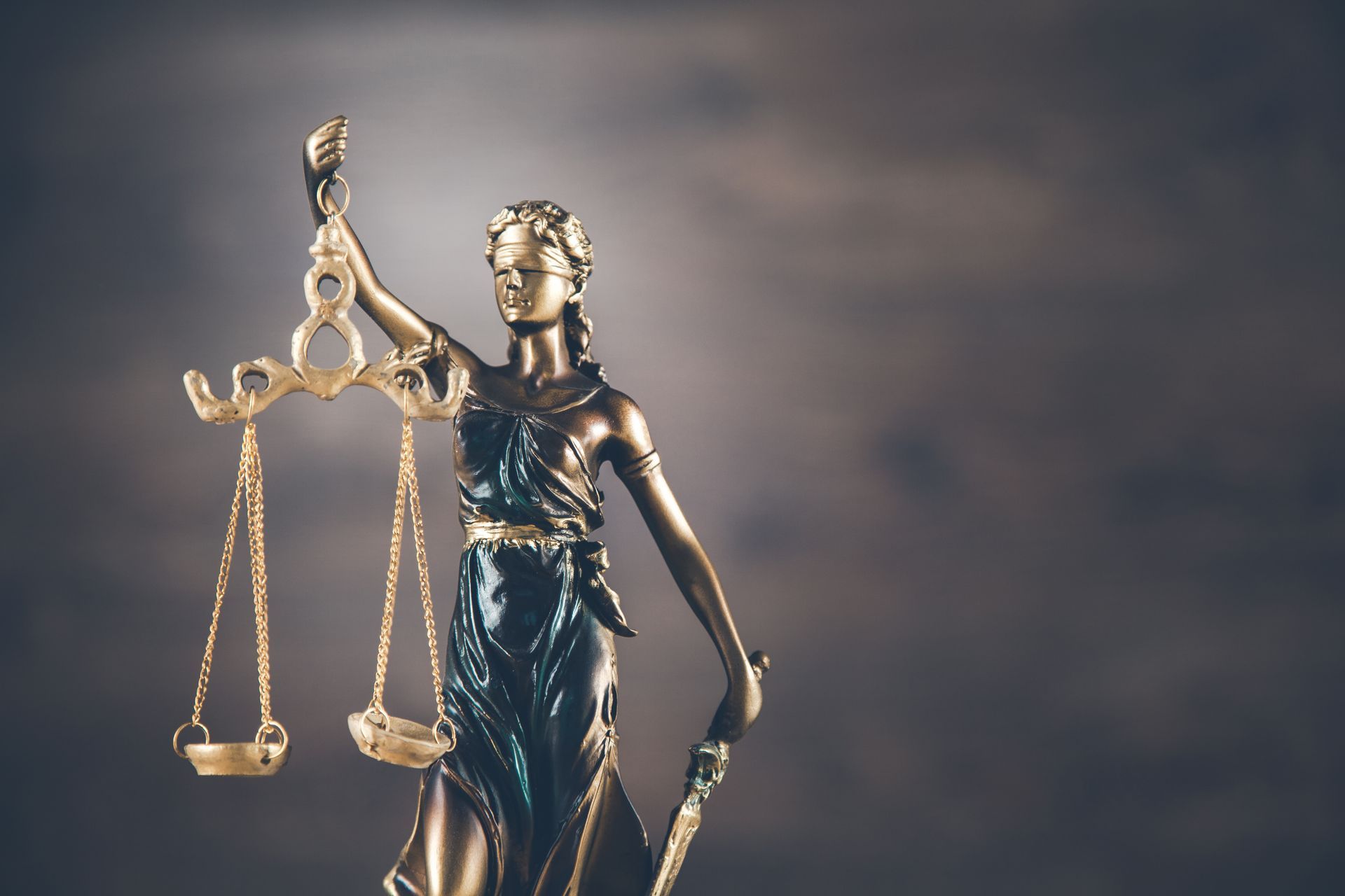 Bronze Lady Justice statue holding scales against a blurred dark background