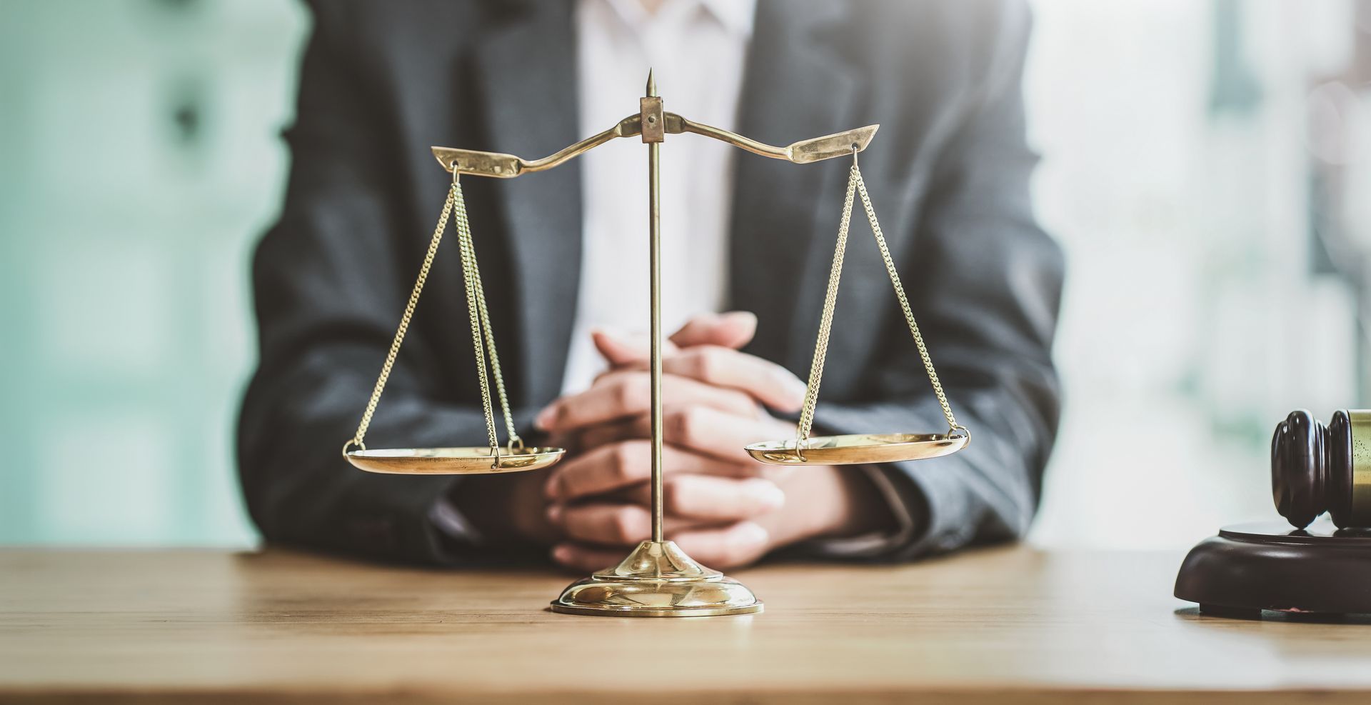 Golden scales on a table with a blurry lawyer in the background. Golden scales on a table with a blurry lawyer in the background.
