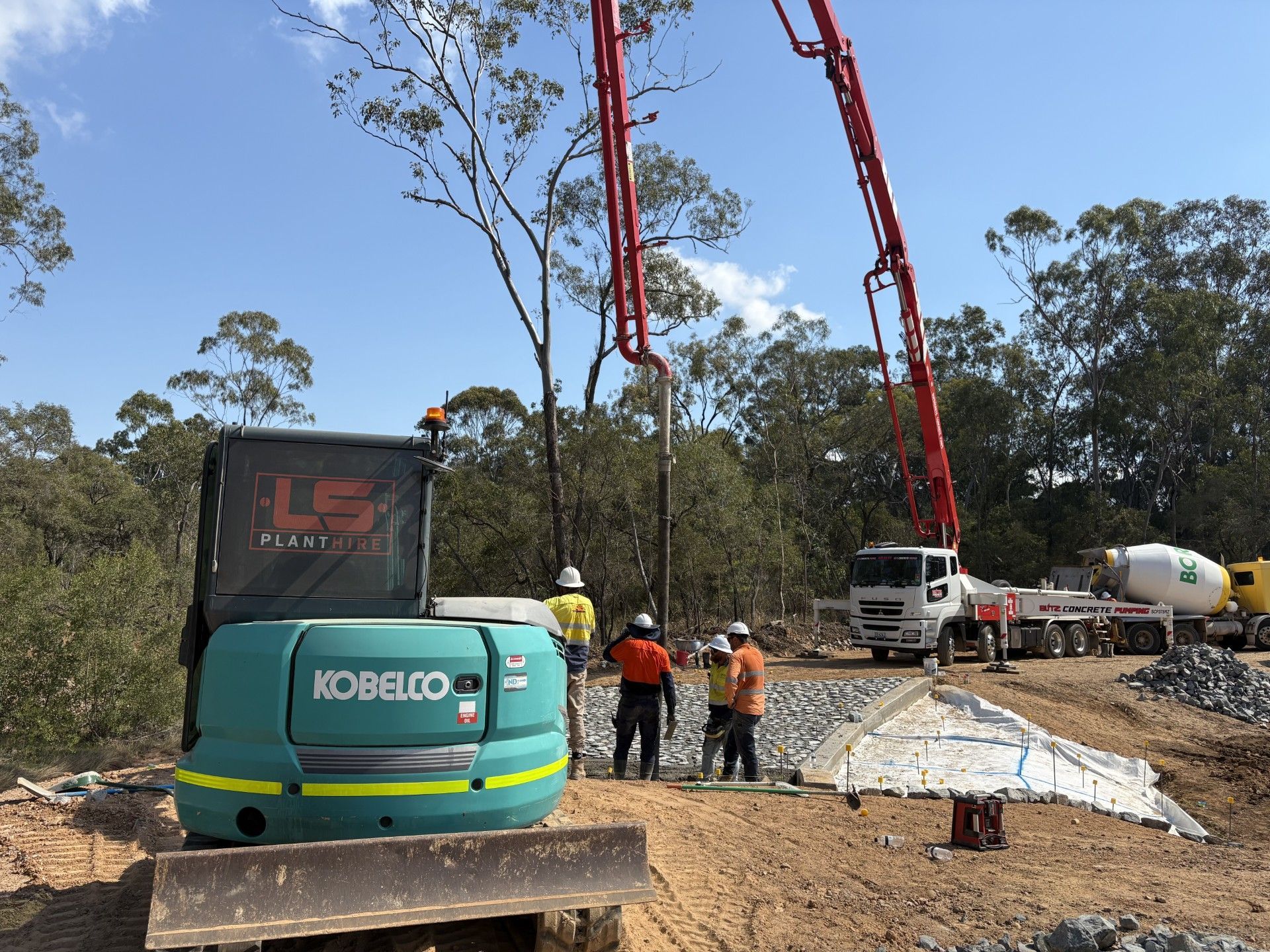 Workers operate a concrete pump truck at a construction site with a green Kobelco excavator in the foreground. — LS Plant Hire in Calliope, QLD