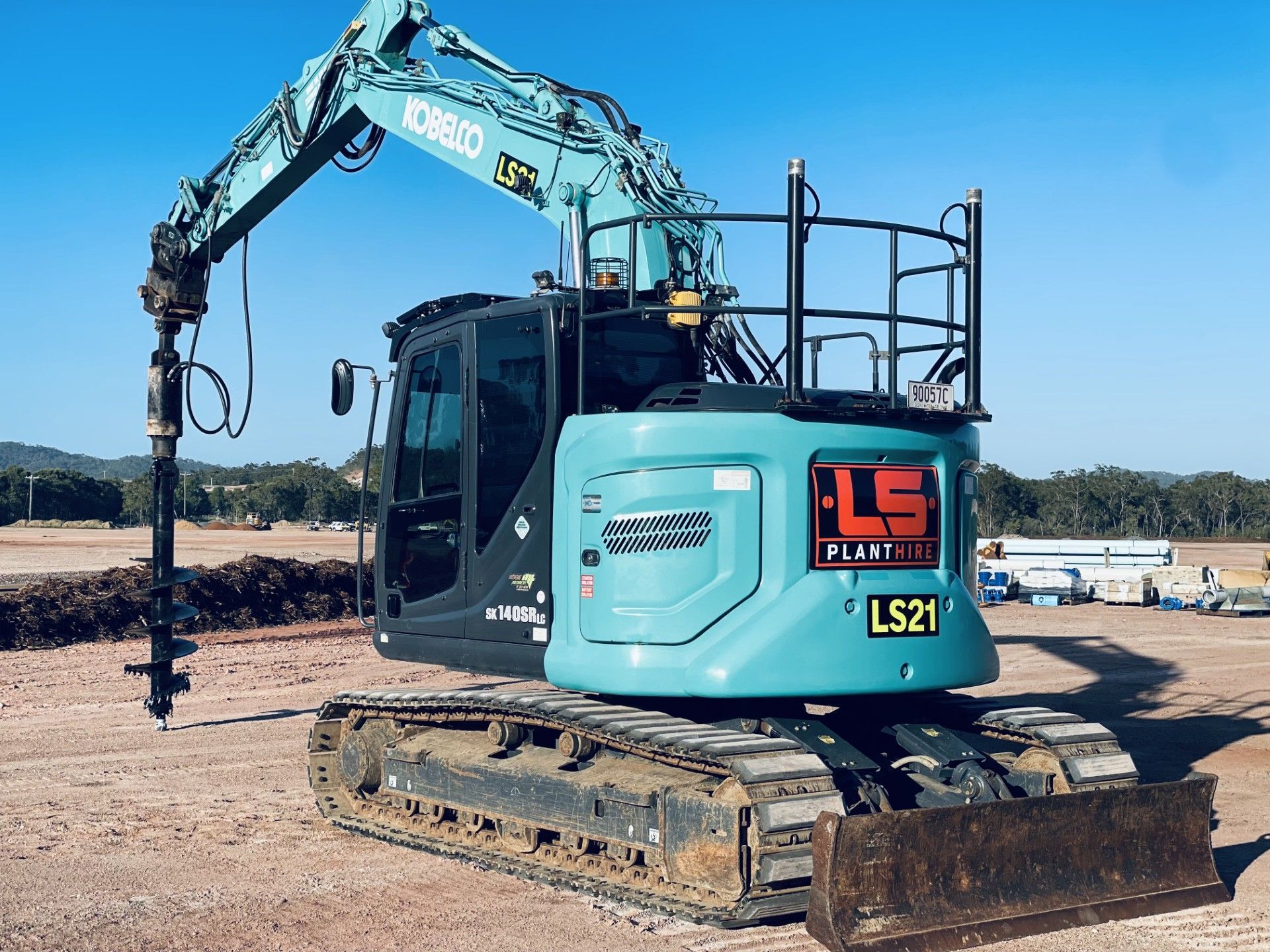 A teal Kobelco excavator with a drilling attachment and