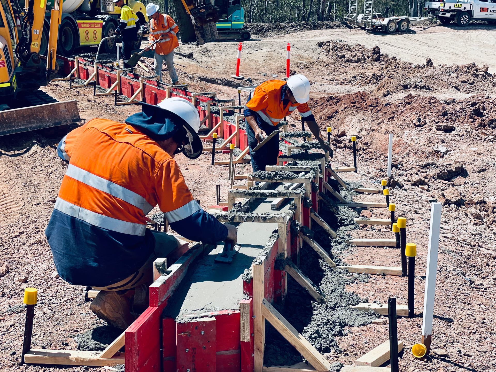 Workers in high-visibility orange gear smoothing wet concrete in wooden forms at a construction site. — LS Plant Hire in Calliope, QLD