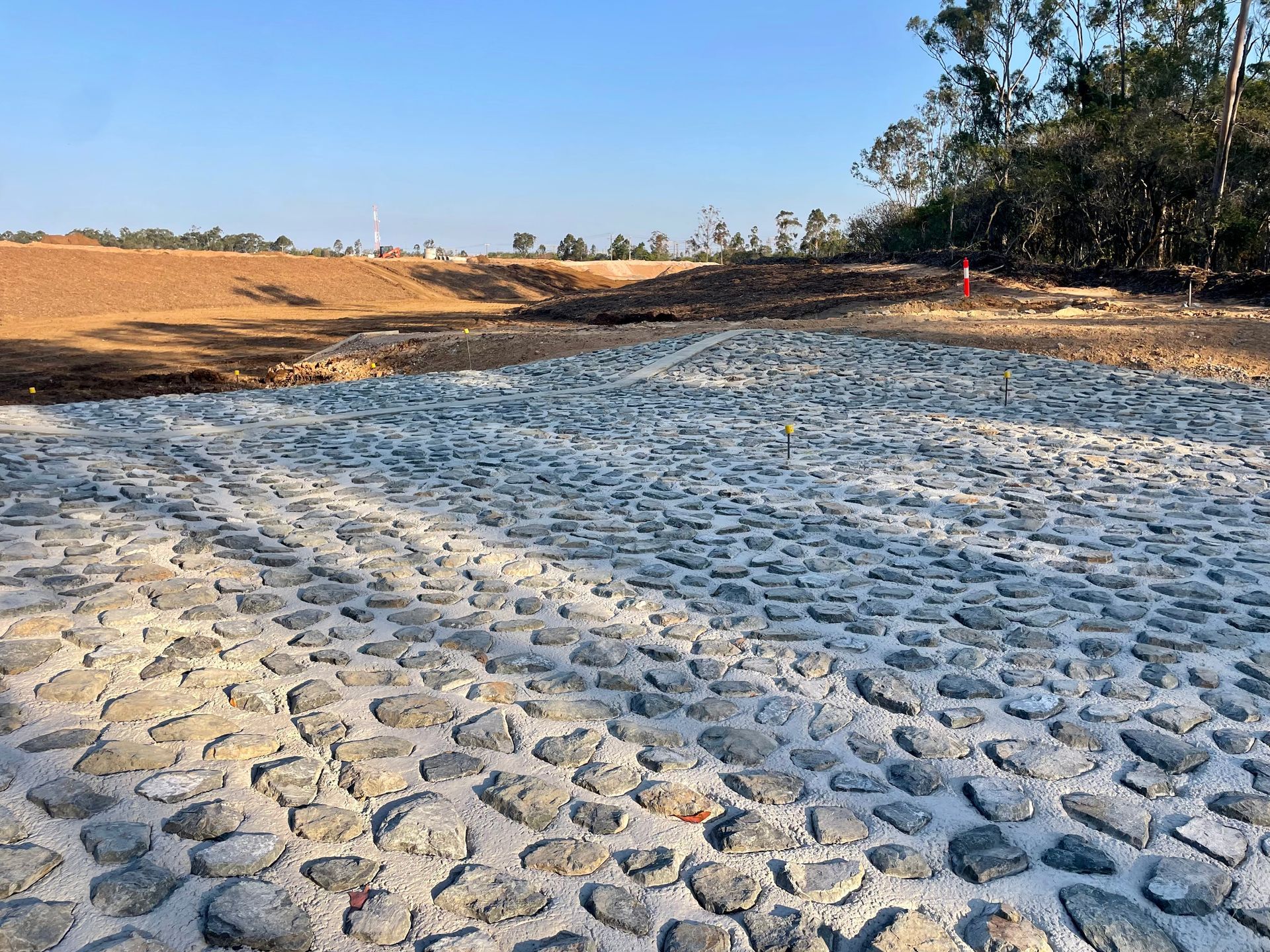 A paved stone surface with grout lines stretches toward an excavated earth bank under a clear blue sky — LS Plant Hire in Calliope, QLD