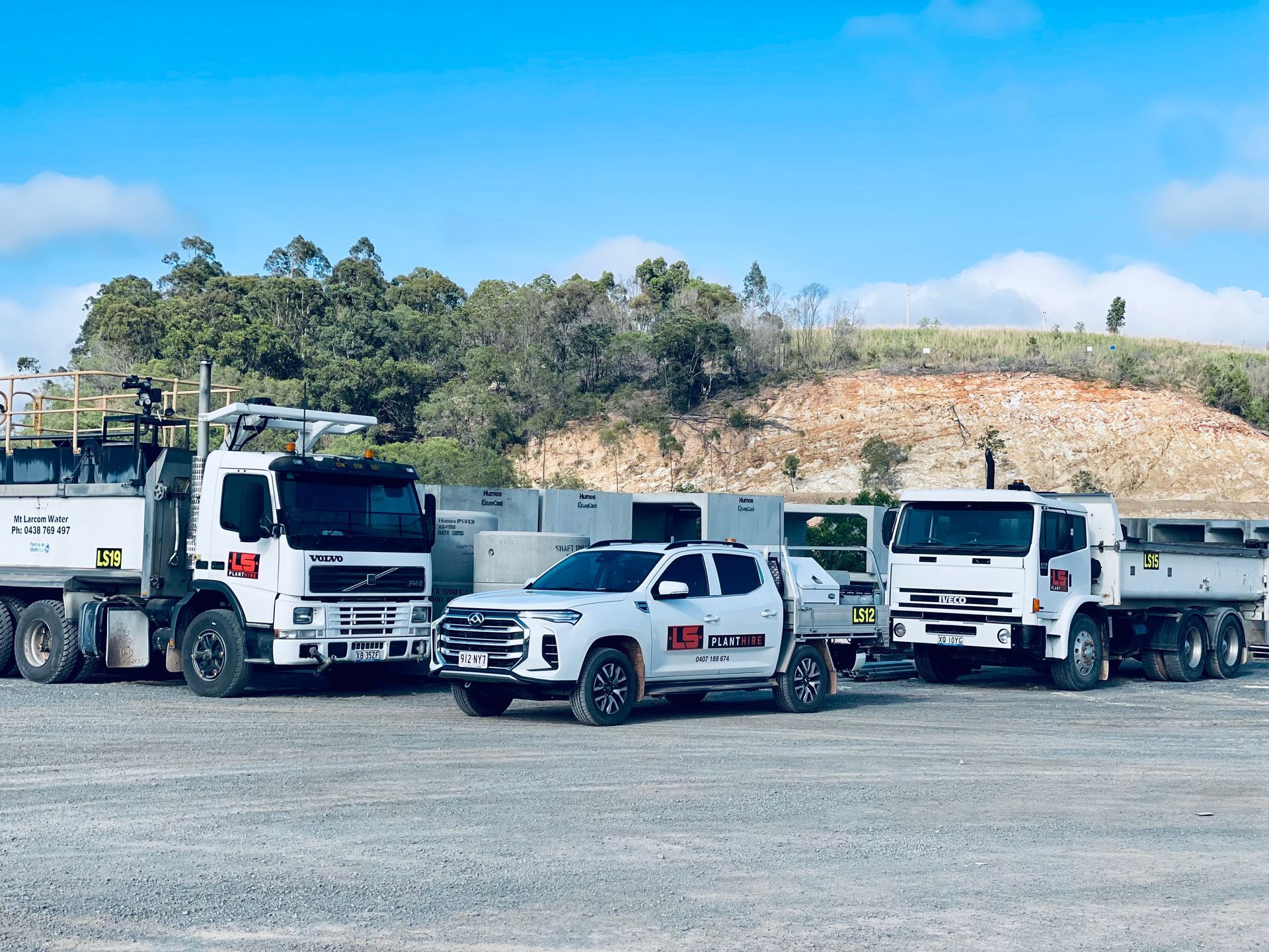 A white pickup truck parked between two large white construction dump trucks on a gravel lot under a clear blue sky. — LS Plant Hire in Calliope, QLD