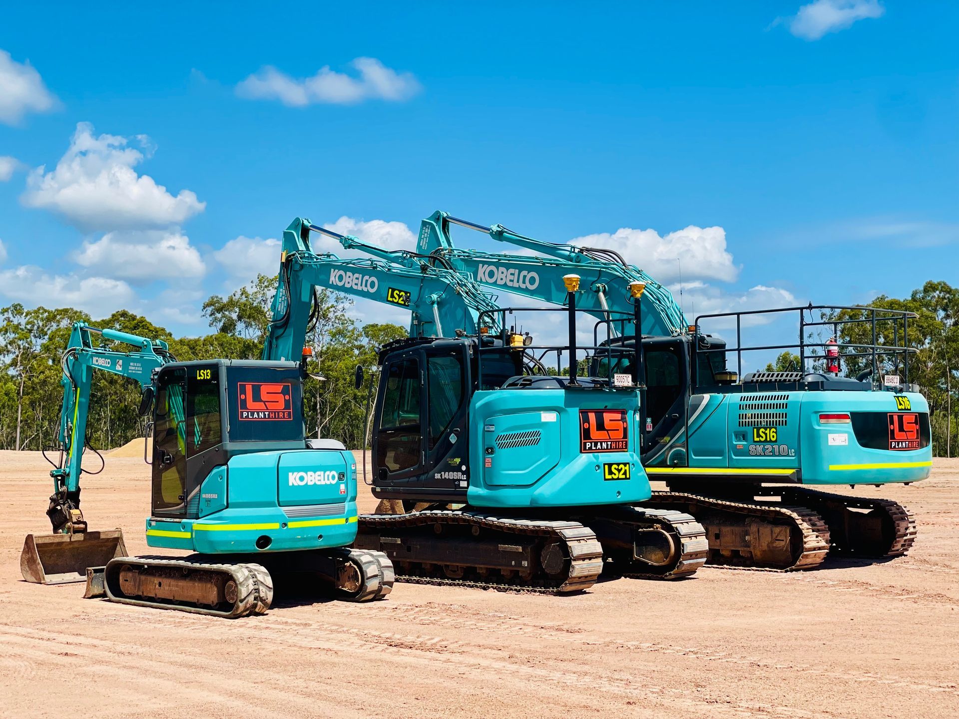 Three turquoise Kobelco excavators parked in a row on a dirt lot under a bright blue sky. — LS Plant Hire in Calliope, QLD