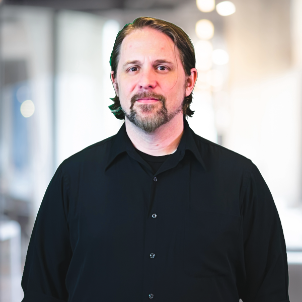 Man with a beard in a black shirt, indoor setting, looking at the camera.