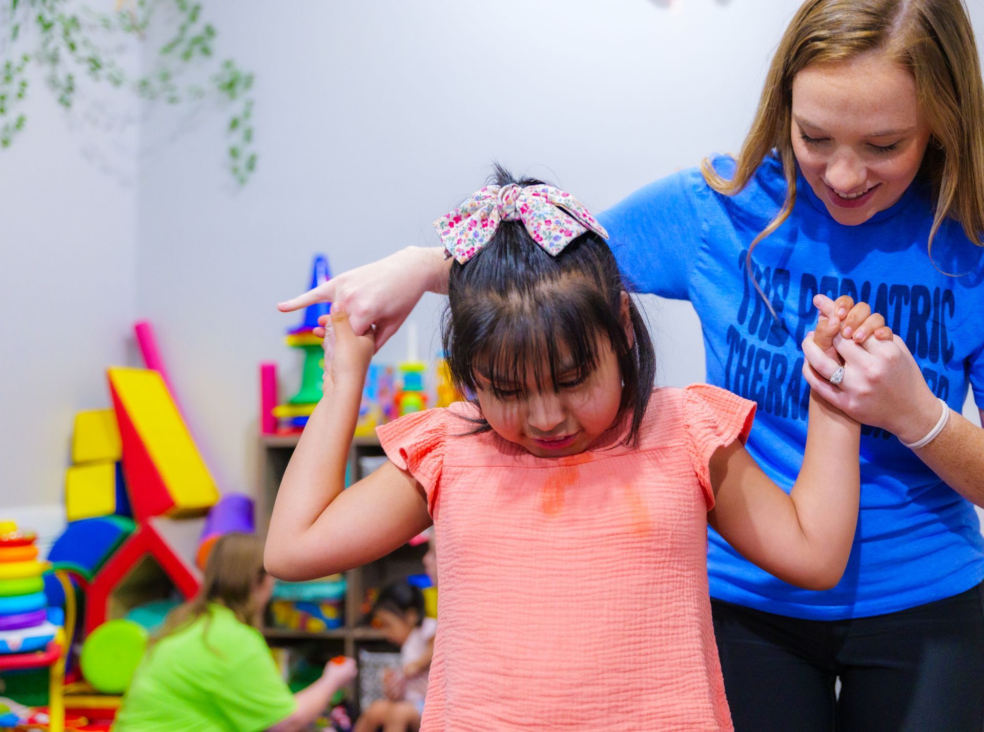 A woman in a blue shirt is helping a little girl with her hair.