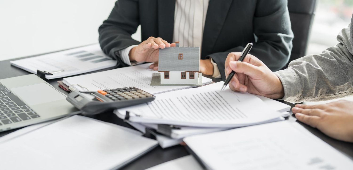 Business meeting with documents, laptop, calculator, and house model on a desk