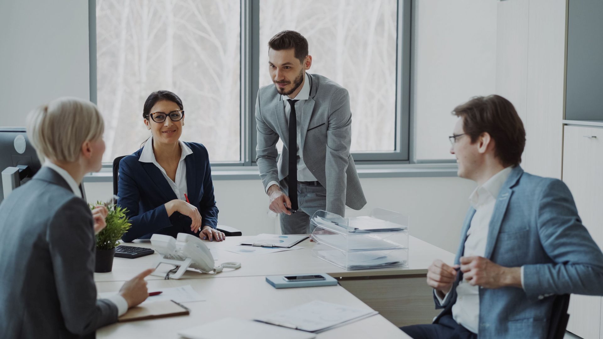 Business meeting in a bright office, with four people discussing documents around a conference table.