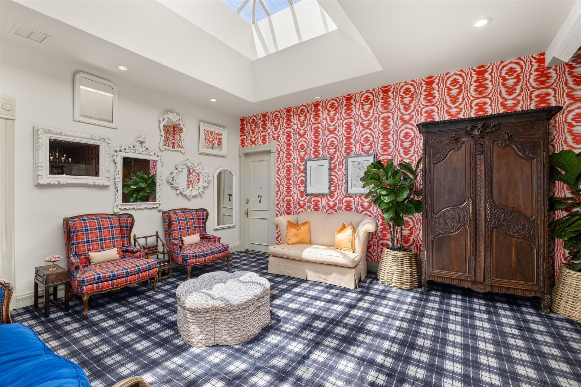 Living room with patterned carpet, red wallpaper, and ornate wooden cabinet. Skylight, seating, and decorative mirrors.
