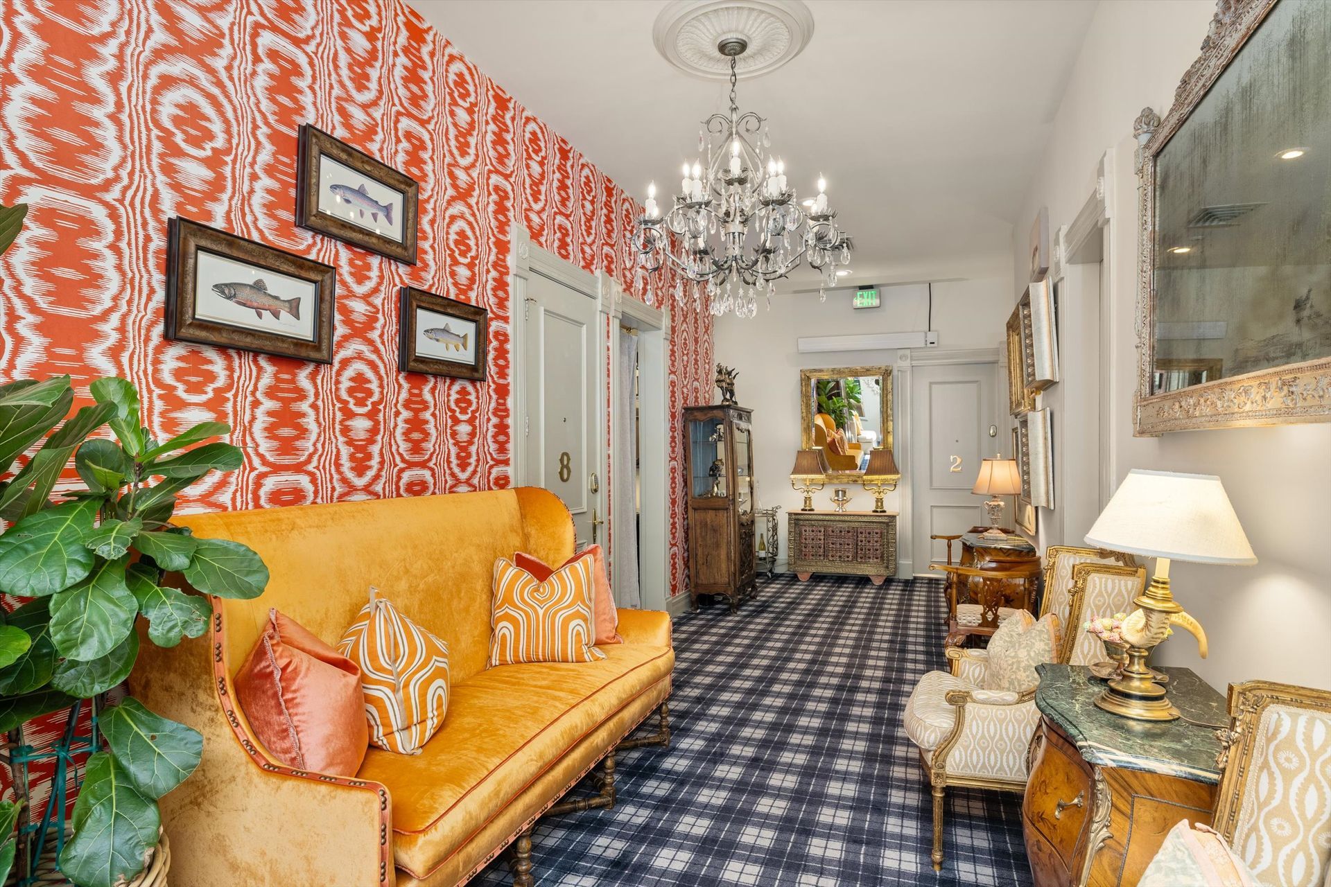 Hallway with patterned wallpaper, yellow couch, and crystal chandelier.