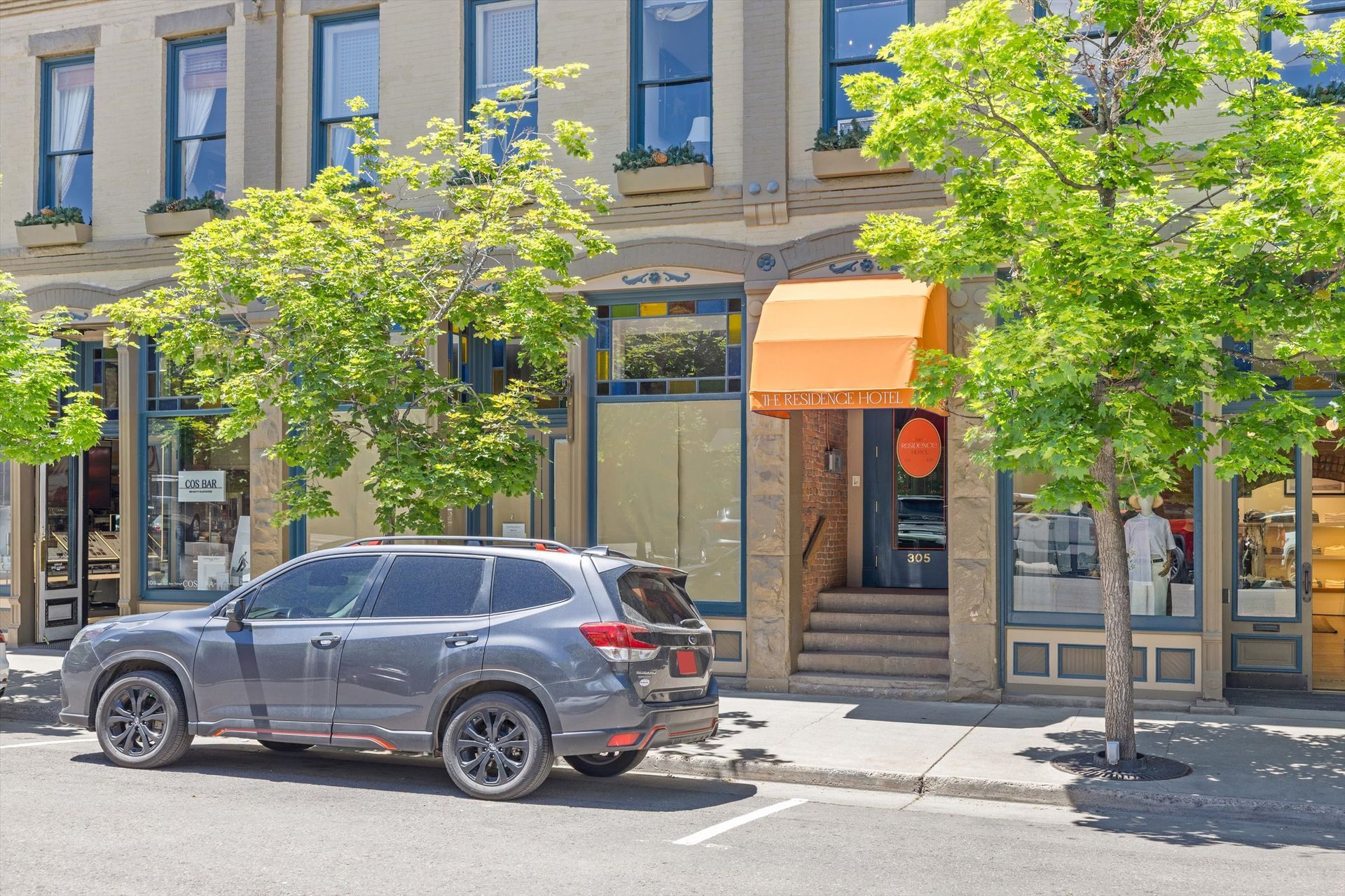 Gray SUV parked on a street in front of shops with awnings and trees.