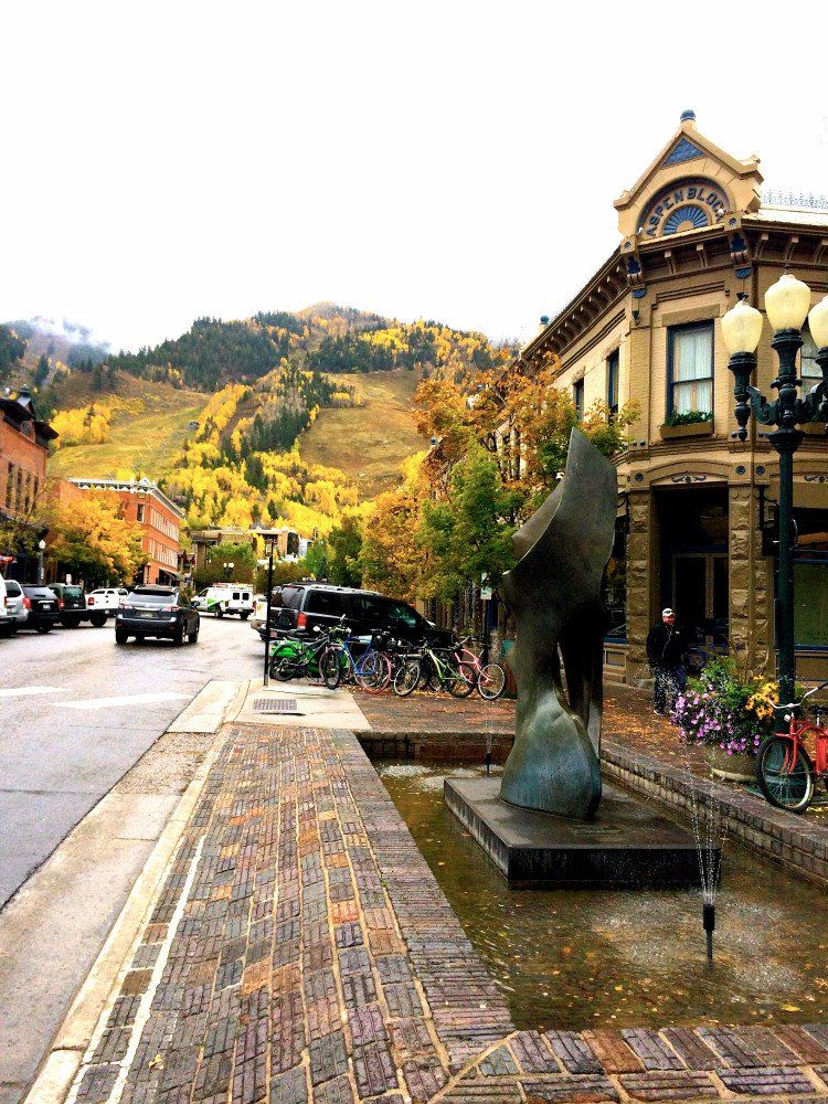 Street scene in Aspen, Colorado, with sculpture, brick sidewalk, and building with mountain in the background.