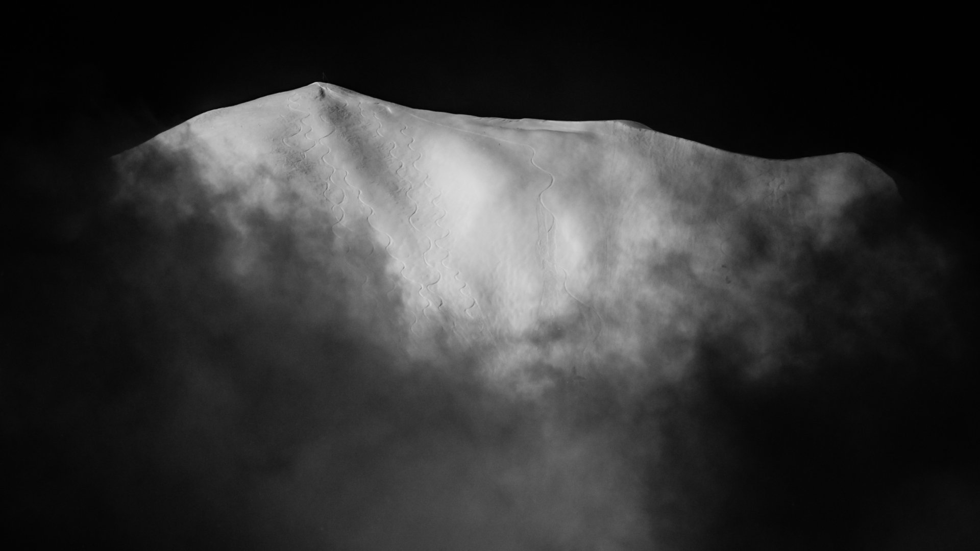 A mountain peak emerging from thick, low-lying clouds, in monochrome.