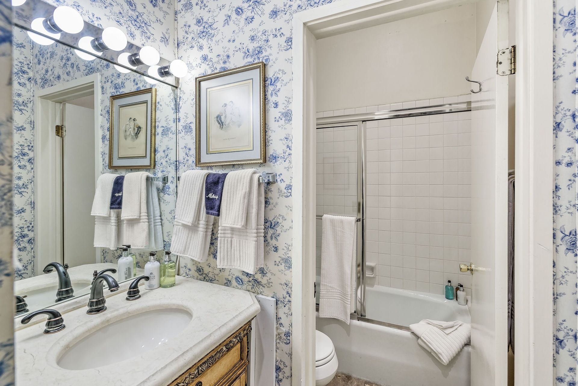 Bathroom with blue floral wallpaper, marble vanity, and tub/shower.