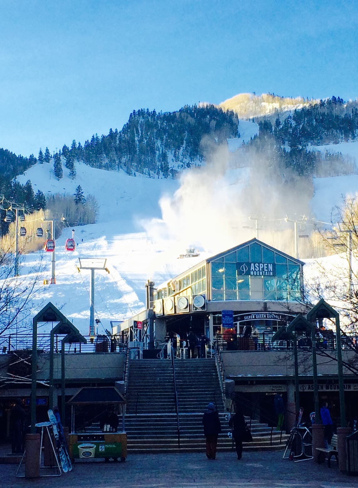 Snowy ski resort with building, lift, and mountain in the background. Bright blue sky.