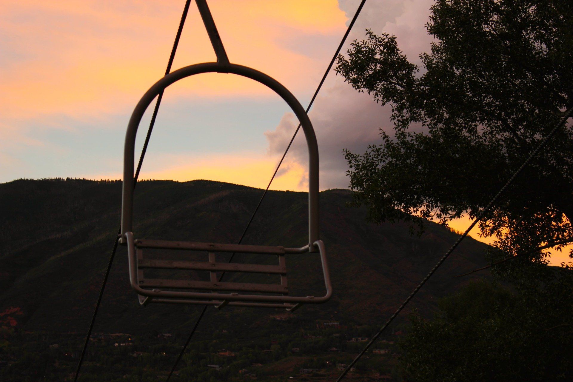 Ski lift chair against a sunset sky over a mountain range.