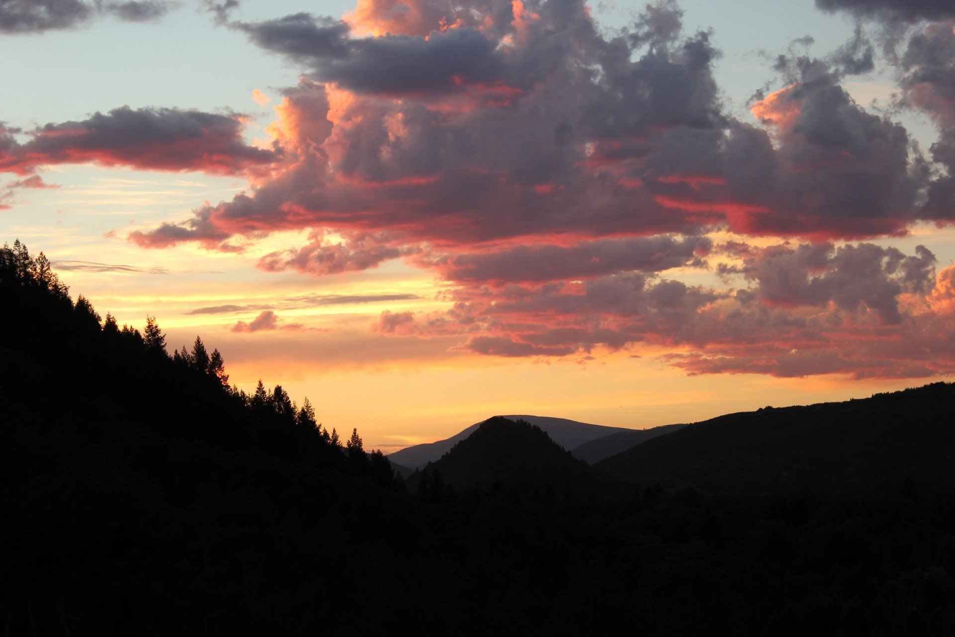 Sunset over silhouetted mountains, with vibrant orange and pink clouds.