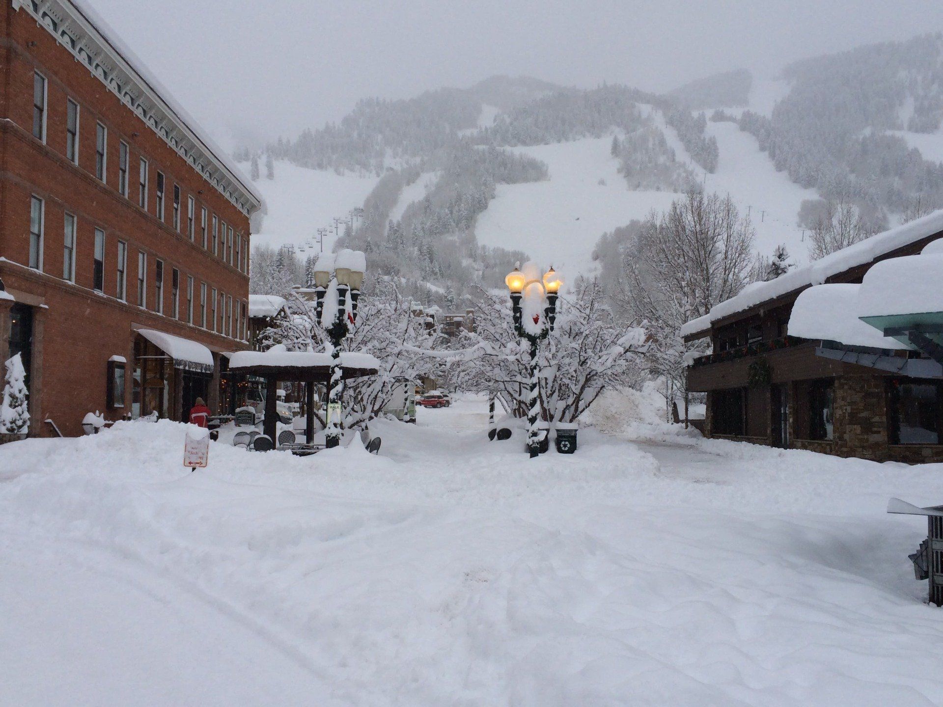 Snowy street scene in front of brick building with mountain in the background.