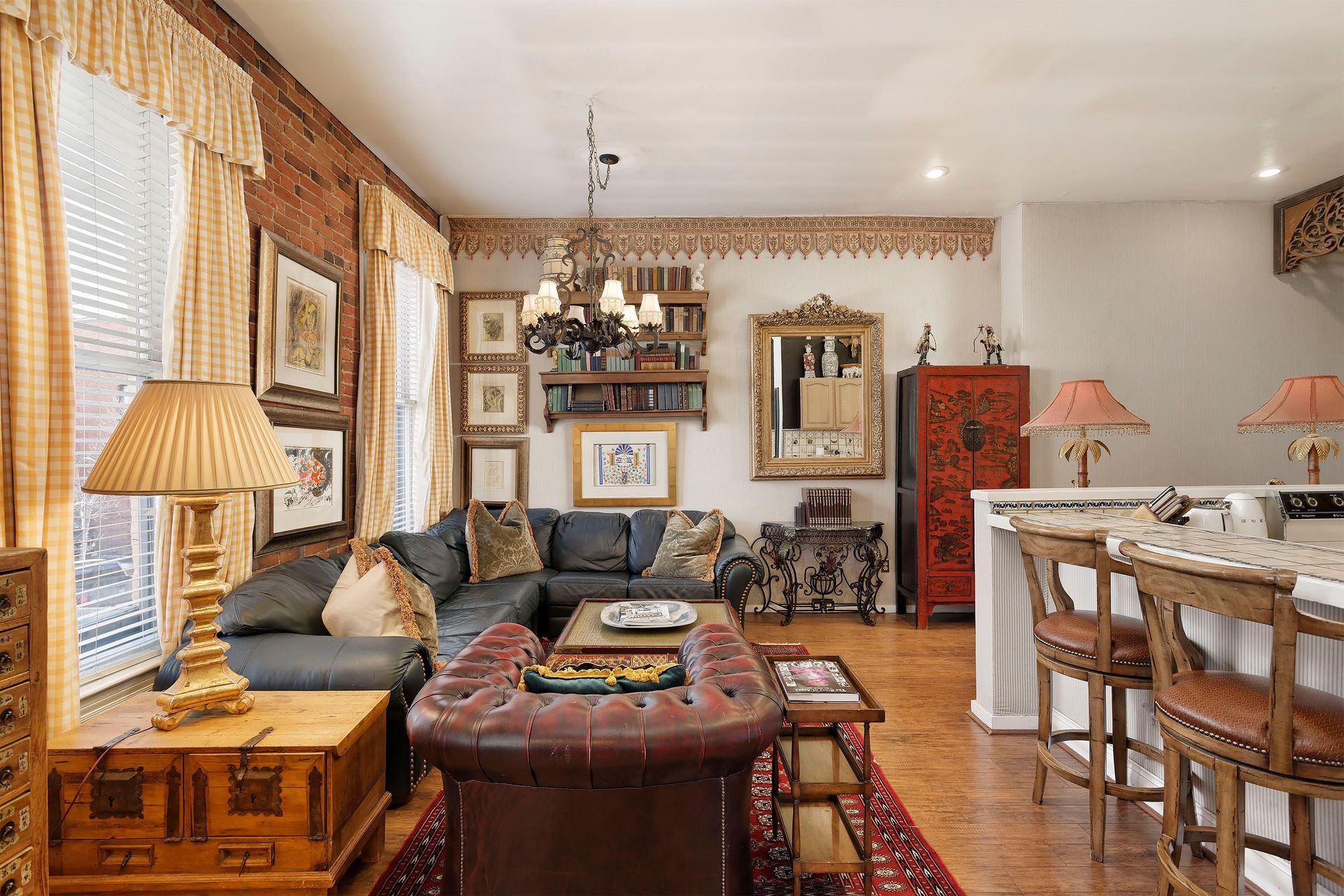 Living room with leather furniture, exposed brick wall, ornate mirror, and bar stools.