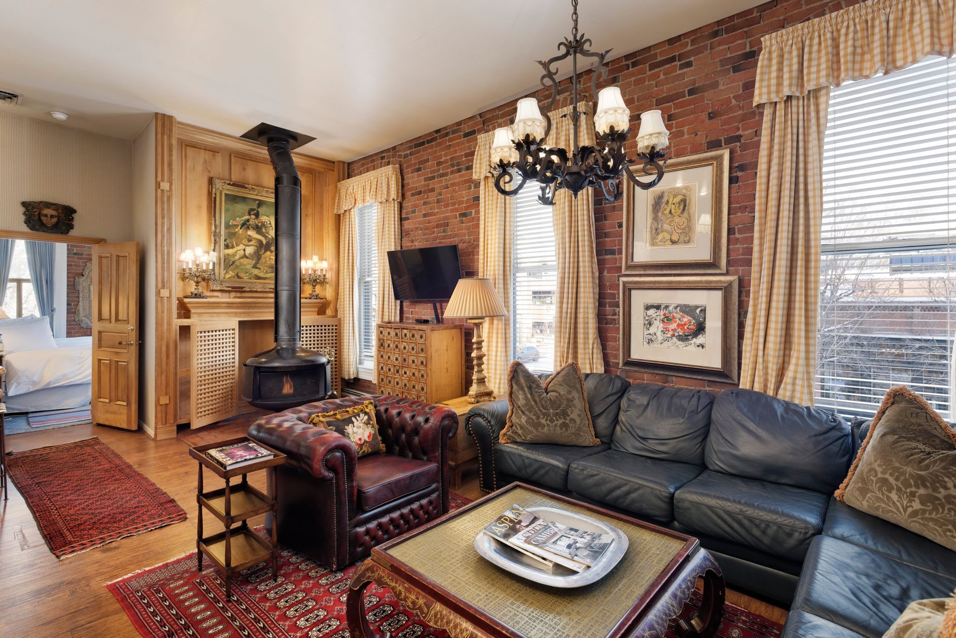 Living room with brick wall, leather furniture, fireplace, and antique chandelier.