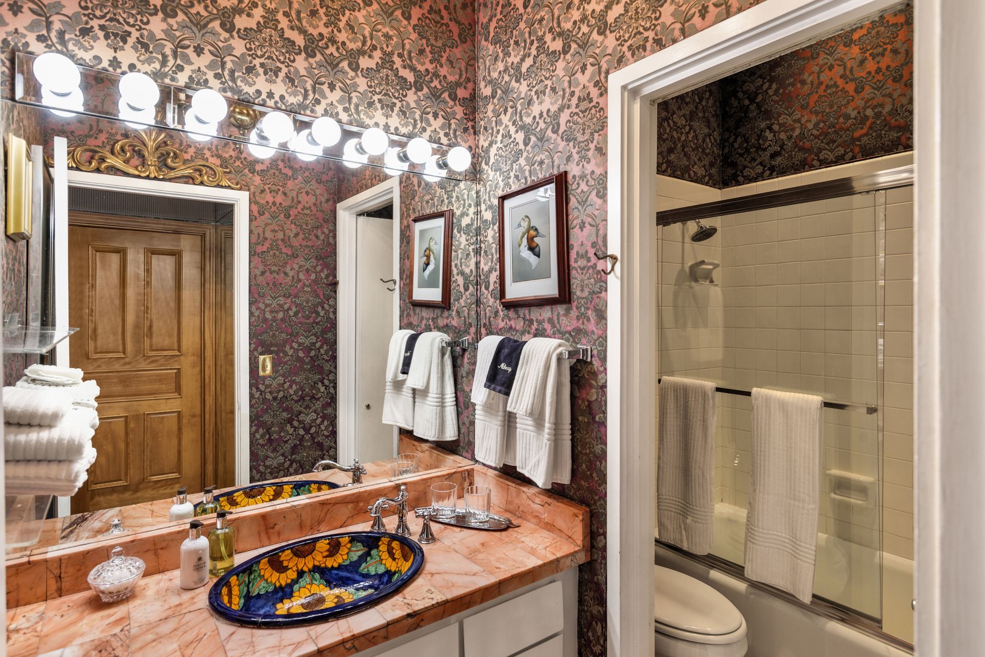Bathroom with floral wallpaper, a sink with an oval ceramic basin, and a door to a shower/tub.