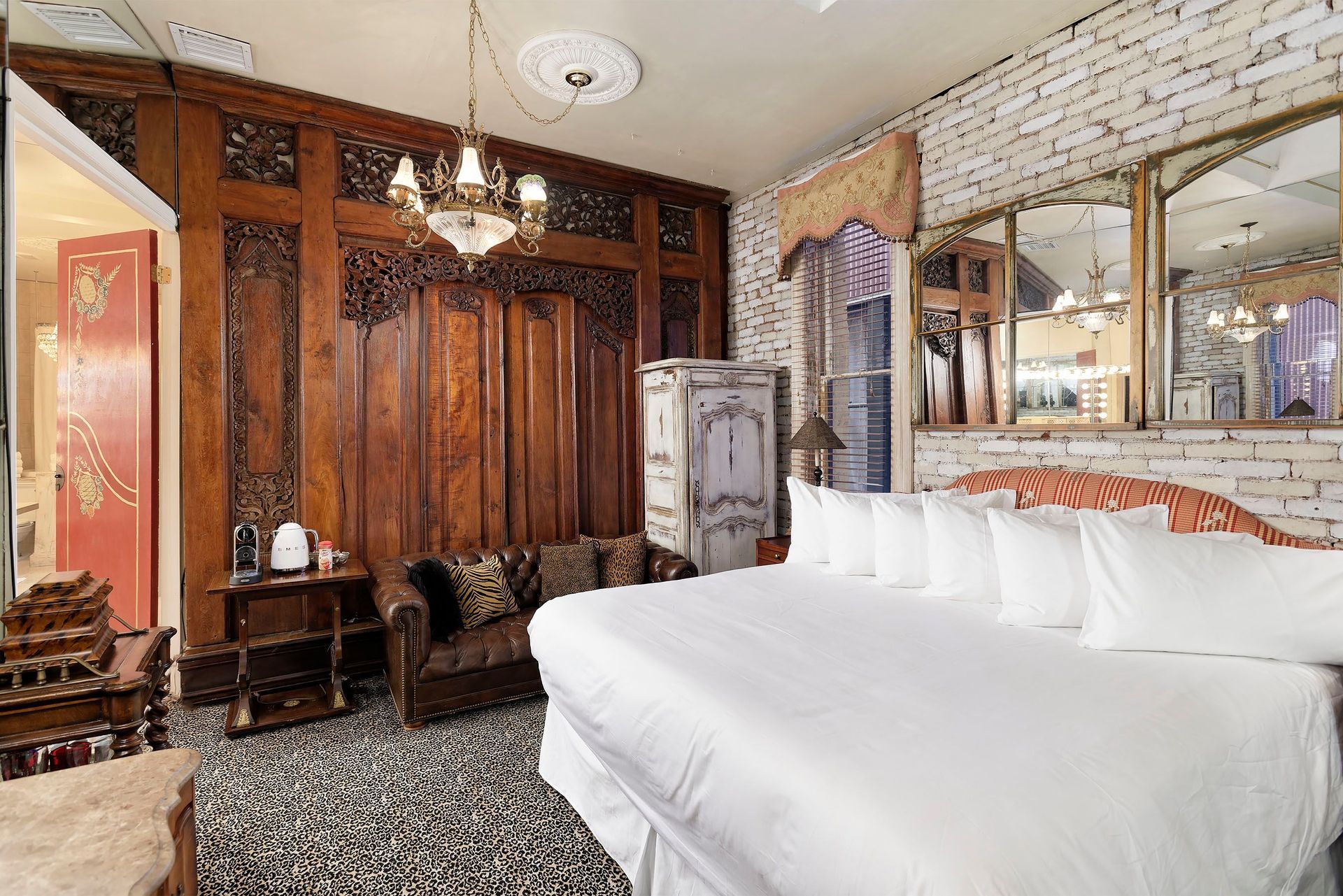 Ornate bedroom with carved wood paneling, white brick wall, four-poster bed, sofa, and chandelier.