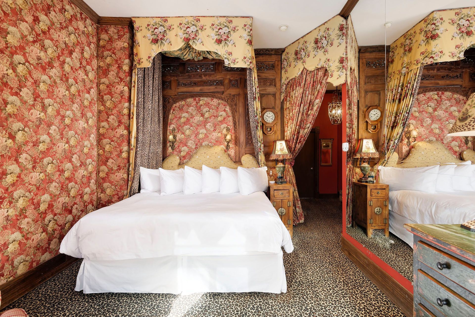 Ornate bedroom with floral wallpaper, canopy bed, patterned floor, and large mirror.