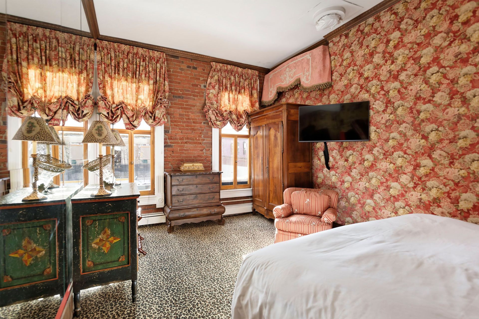 Bedroom with patterned wallpaper, brick wall, wood furniture, and a bed.