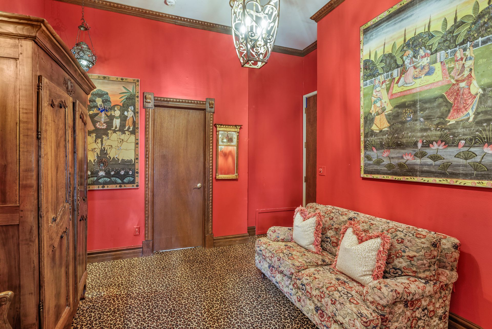 Red-walled hallway with floral-patterned sofa, wooden cabinet, artwork, and textured flooring.