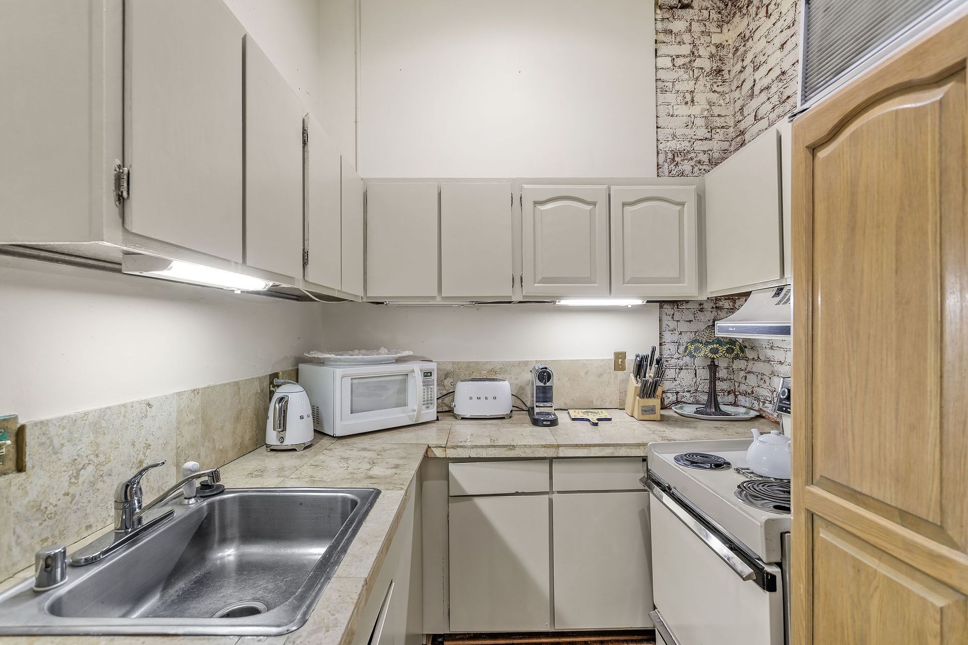 Small kitchen with cream-colored cabinets, stainless steel sink, and appliances.