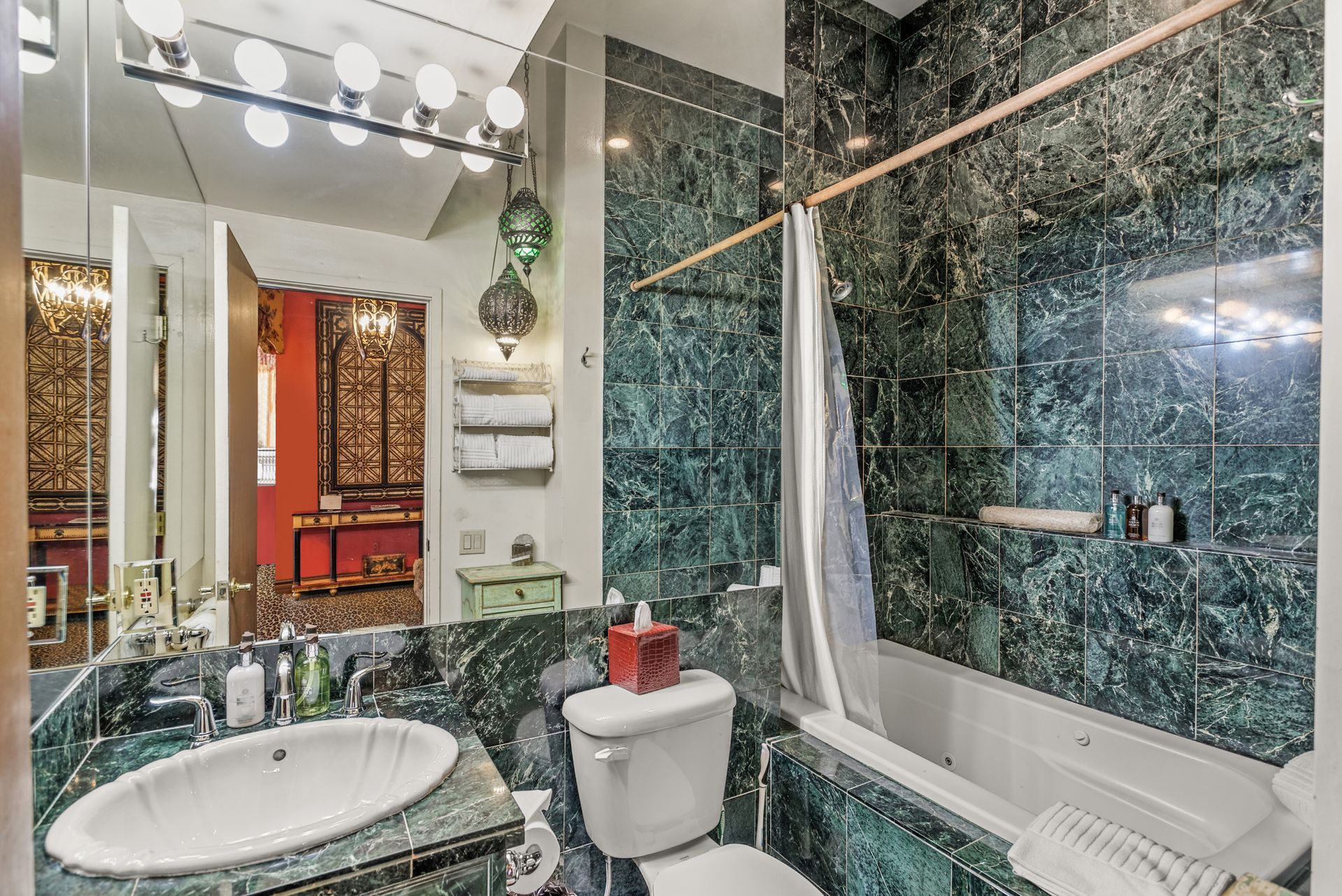 Bathroom with green marble tile, a white sink, and a toilet. The mirror reflects a glimpse of another room.