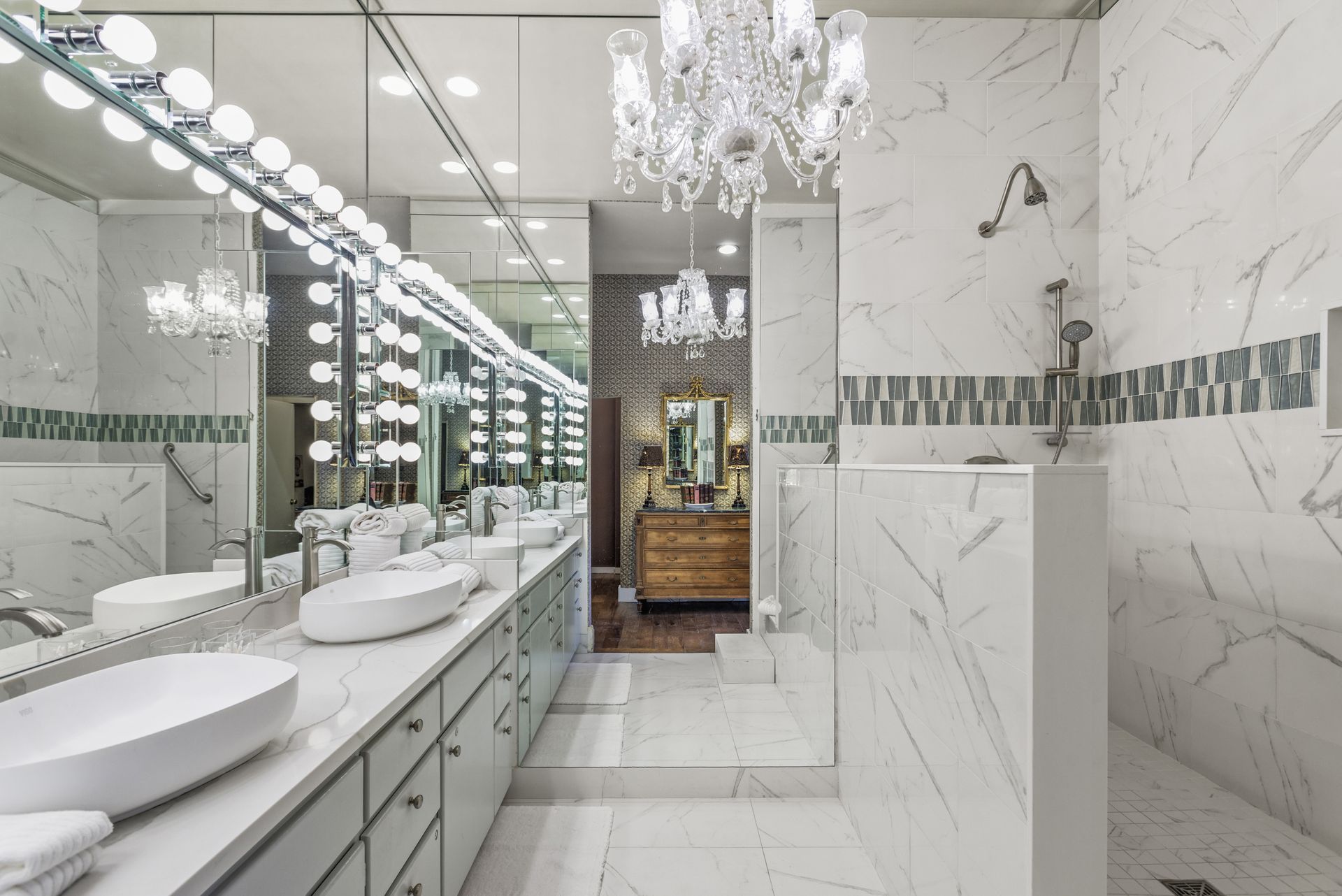 Luxurious bathroom with marble walls, double vanity, and chandelier.