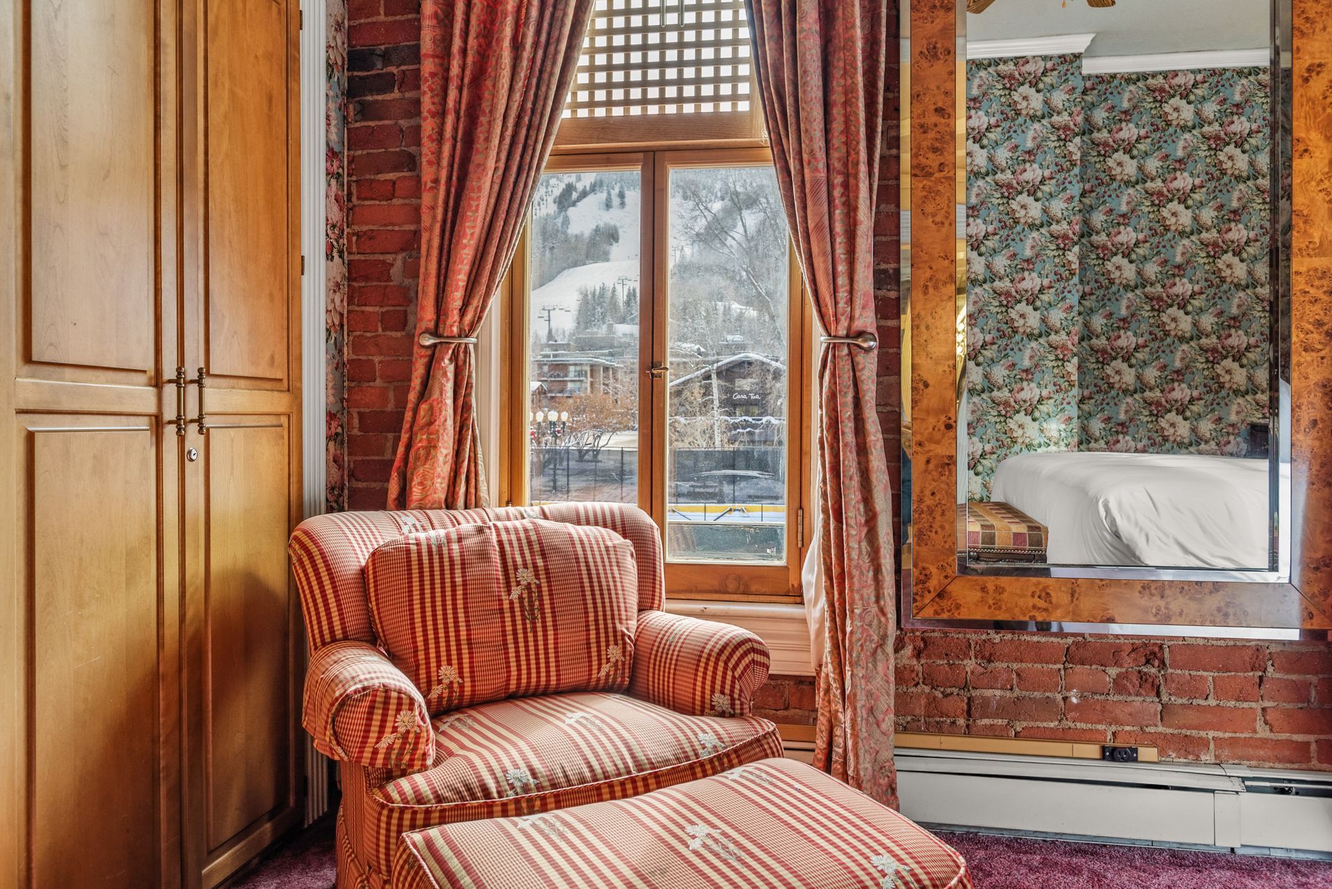 Cozy room with red striped armchair, brick wall, window overlooking snow-covered landscape, large mirror.